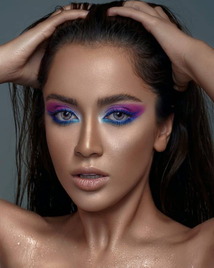 mujer con aspecto de sombra de ojos azul y púrpura y acabado de maquillaje resplandeciente